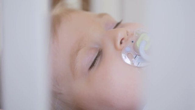 A little girl is sleeping in a baby crib with a pacifier in her mouth