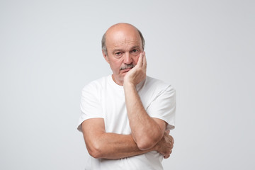 Closeup portrait of sleepy mature man in white t-shirt, funny guy placing head on hand, unhappy looking at camera.