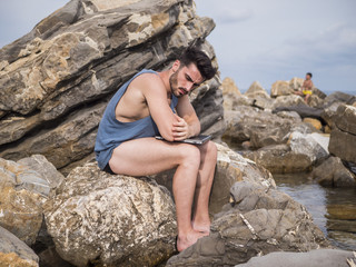 Young handsome man working on laptop computer, typing on keyboard while at the beach in front of the sea