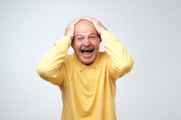 mature hispanic man in yellow shirt celebrating victory of his team over gray background.
