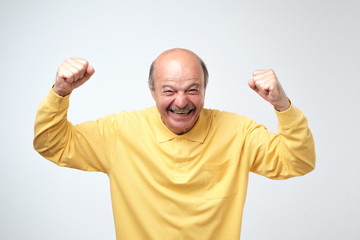 mature hispanic man in yellow shirt celebrating victory of his team over gray background.