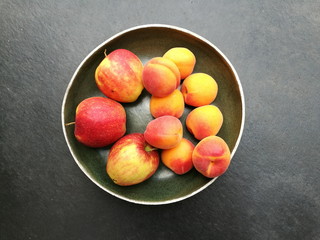 Runde Obstschale mit Äpfeln und Pfirsichen in Rot und Orange auf grauem Betonboden in einer...