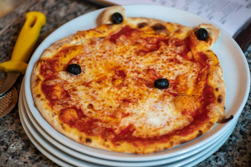 Kinder Margarita Pizza mit Gesicht aus dem Pizzaofen auf einem Teller und in einer Schachtel