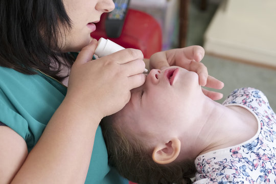 Mother administering medication eye drops to young daughter at home