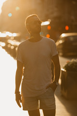 A young man with beard posing with his sunglasses in the orange rays of the sunset on the old European street in Spain