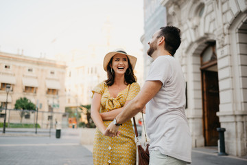 Awesome brunette girl in the hat with her boyfriend with beard laughing together on the old European street in Spain on the sunset