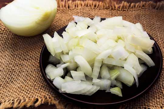 Finely chopped white onions on a round plate next to the half head, all on a linen cloth napkin.