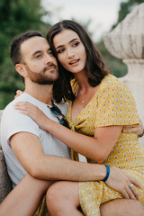 Stylish brunette girl sitting on the knees of her boyfriend with beard on the ancient bridge in Spain in the evening. Close portrait 