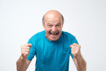 mature hispanic man in blue t-shirt celebrating victory of his team over gray background.