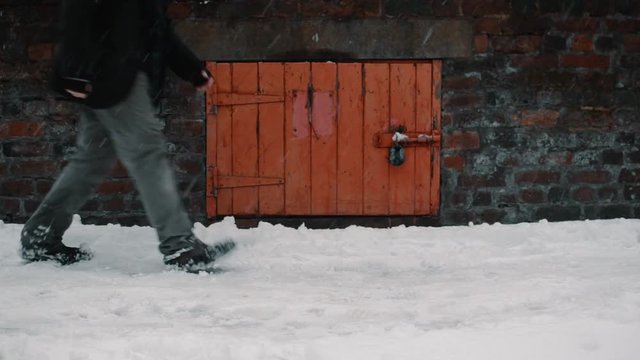 Male legs walking in snow with small red door behind
