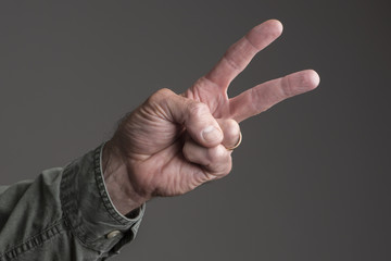Isolated man's hand, two fingers up in peace sign.  Green canvas shirt buttoned at the cuff.  Dark grey background.