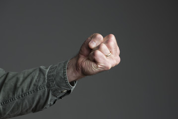 Isolated man's fist.  Arm in green canvas shirt.  Grey background.