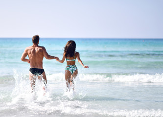 Happy cheerful couple hold hans and running in the sea together. Romantic vacation, honeymoon love