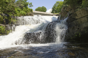 Waterfall Cascading Over Steep Bedrock Cliff Into Whitewater Stream