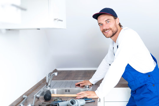 Installateur / Klempner positiv lächelnd bei der Arbeit in einer Küche 