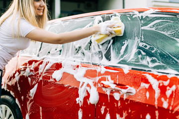 Young woman washing her car with sponge.