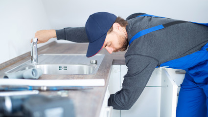 Installateur im Blaumann arbeitet an einem Waschbecken 
