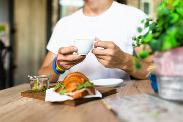 Man eating croissant sandwich and drinking coffee in a cafe bar and restaurant.