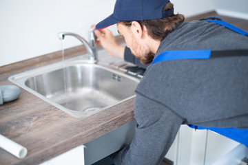 Installateur im Blaumann arbeitet an einem Waschbecken 