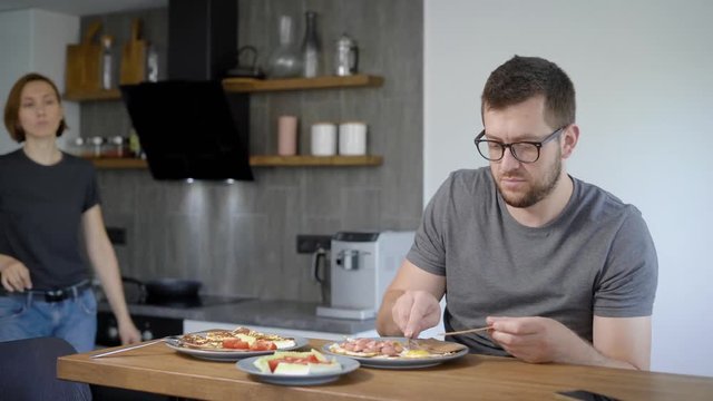 Husband and wife eat breakfast together. Behind the wooden bar, behind the modern kitchen interior.