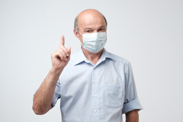 Mature man in protective mask pointing finger up.