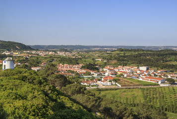Fototapeta na wymiar Scenic view of the valley from wall of fortress. White houses red tiled roofs Beautiful old town with medieval. Obidos village, Portugal. Summer sunny day.