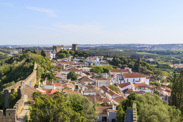Scenic view of white houses red tiled roofs, and castle from wall of fortress. Beautiful old town with medieval. Obidos village, Portugal. Summer sunny day.