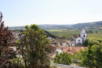 Scenic view of the valley from wall of fortress through orange trees . White houses and red tiled roofs. Beautiful old town with medieval. Obidos village, Portugal.