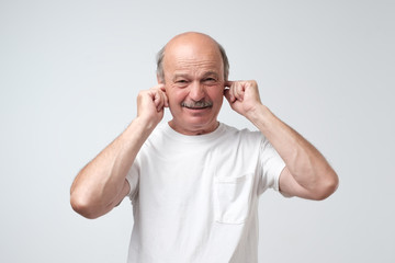 Mature man in white tshirt suffering from loud music and pain screaming trying to plug ears against...