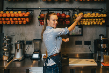 Happy young female bartender standing at juice bar counter and working.