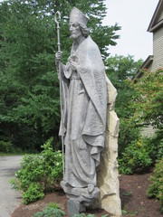 A stone statue of Saint Patrick with trees and plants in the background 