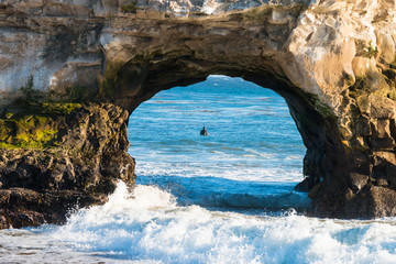 View of a surfer through a hole in the rock (Santa Cruz)