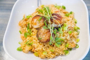 Tasty risotto with Gulf Shrimp, crawfish tails, seared scallops, fresh herbs vegetables on a white plate