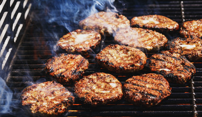 Preparing delicious hamburgers on the outdoor grill for family lunch. Conceptual picture of grilled burgers at fire flame. Hamburger patties turn over on the grill.