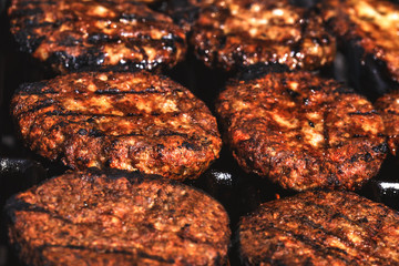 Appetizing hamburgers grilled on the outdoor grill in front of american restaurant. Conceptual picture of finishing cooking a black burger. Hamburger cutlets turn over on the grill.