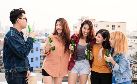 Group of asian women and man drinking at rooftop party, casual outdoors celebration