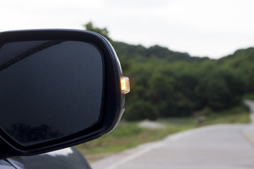 Mirror of car with open light signal and blur road and tree.