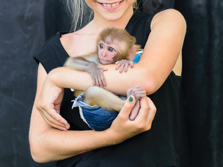 The girl carefully holds a small monkey on her hands.