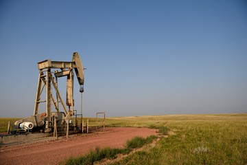 Crude oil pump jack with rural fields and clear blue sky at sunset in Wyoming, with Copy Space.
