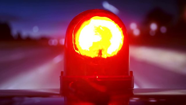 POV driving vehicle with red flash emergency light on highway at night. Rotating warning beacon mounted on car roof closeup.