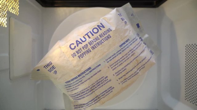Top view making popcorn in a paper bag in the microwave. Popped popcorn bag rotating in microwave oven.