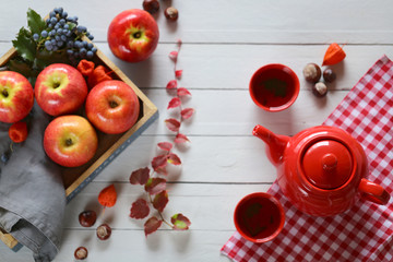 Fototapeta na wymiar Autumn tea.red teapot with a cup of tea,blue tray with red apples, mahonia and chestnuts on a blue wooden background.Autumn season. Autumn time
