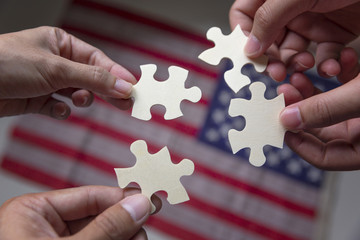 Group of business people assembling jigsaw puzzle and represent team support and help concept with American flag background.
