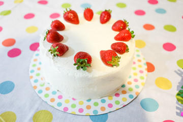 A Fun White Vanilla Cake topped with strawberries on a fun polka dot table cloth, perfect for a birthday celebration.
