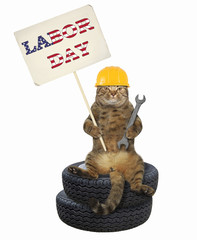 The cat worker in yellow helmet with a wrench is sitting on the pile of tires and holding a banner with the text " labor day ". White background.