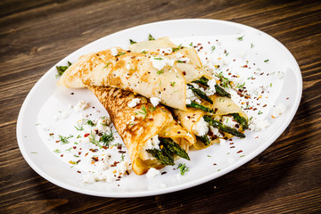 Crepes with spinach and cottage cheese on wooden background 