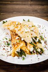 Crepes with spinach and cottage cheese on wooden background 