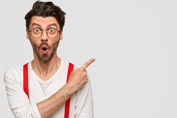 Emotional bearded male has surprised facial expression, astonished look, dressed in white shirt...