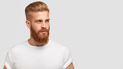 Fototapeta Serious thoughtful male with ginger beard, dressed casually, focused somewhere, isolated over white background with free space on right for your advertising content. Pensive red haired hipster obraz