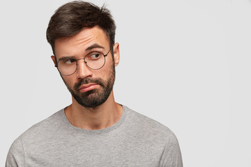 Pensive unshaven attractive male looks thoughtfully aside, has deep thoughts in mind, has round...